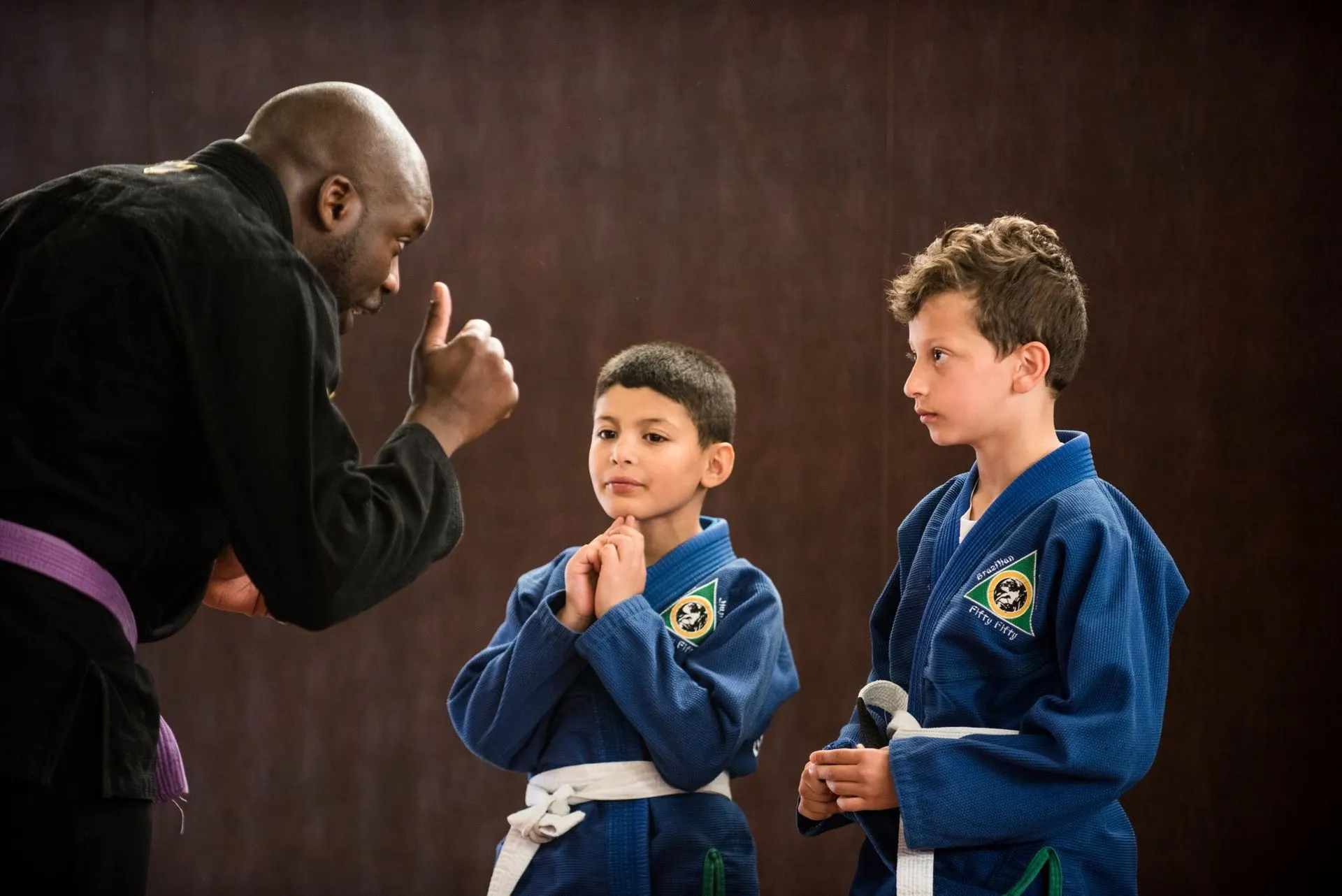 Un coach montre une technique à deux garçons en kimono bleu