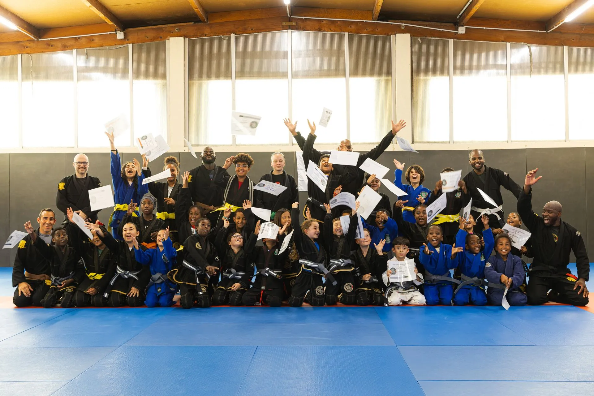 Remise de diplômes : enfants et adultes du club, bras levés sur le tapis